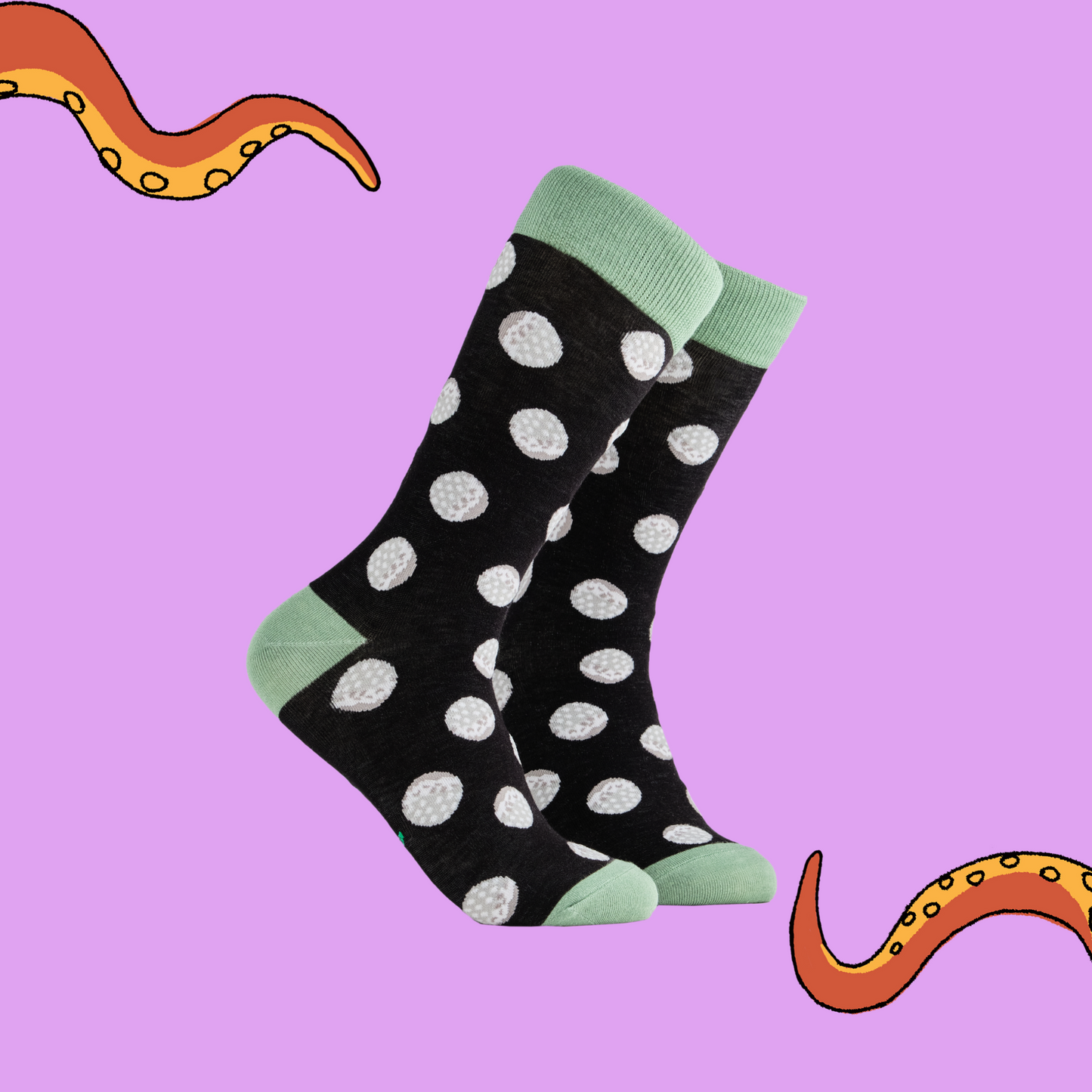 A pair of socks depicting golf balls. Black legs, light green cuff, heel and toe.