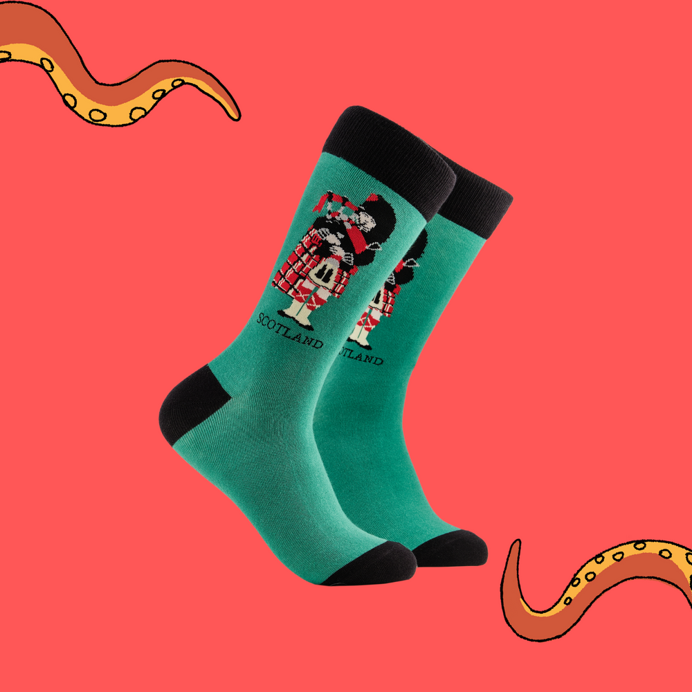 A pair of socks depicting a scotsman playing bag pipes. Green legs, black cuff, heel and toe.