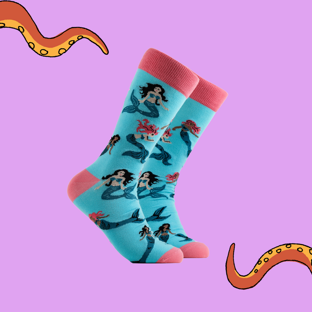 A pair of socks depicting mermaids swimming. Light blue legs, pink cuff, heel and toe.
