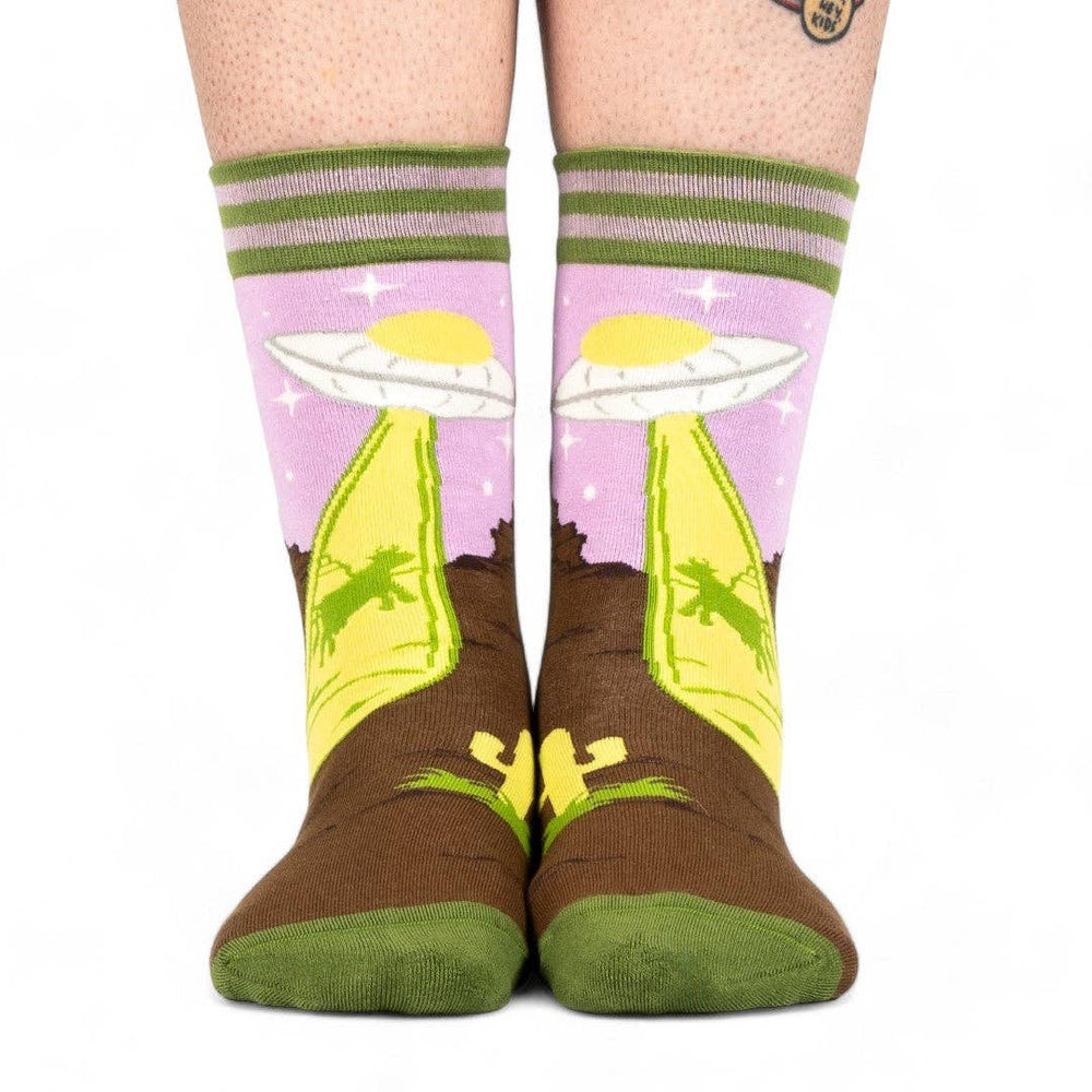 
                      
                        A model wearing a pair of socks featuring a UFO and a very confused cow. Brown legs, green heel, toe and cuff. 
                      
                    