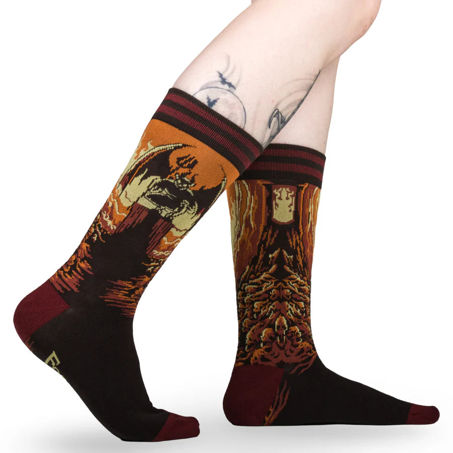 
                      
                        A model wearing a pair of socks featuring a devil on a pile of skulls. Brown legs, red heel, toe and cuff. 
                      
                    