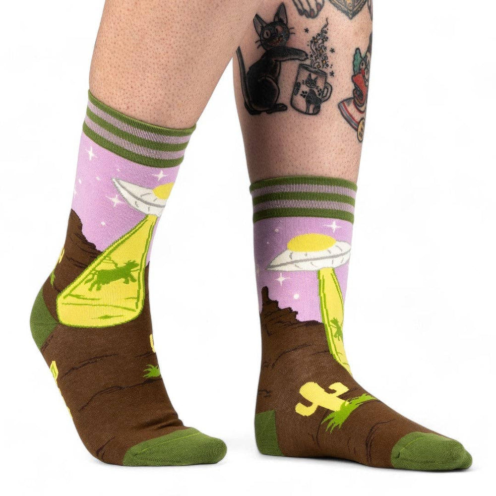 
                      
                        A model wearing a pair of socks featuring a UFO and a very confused cow. Brown legs, green heel, toe and cuff. 
                      
                    