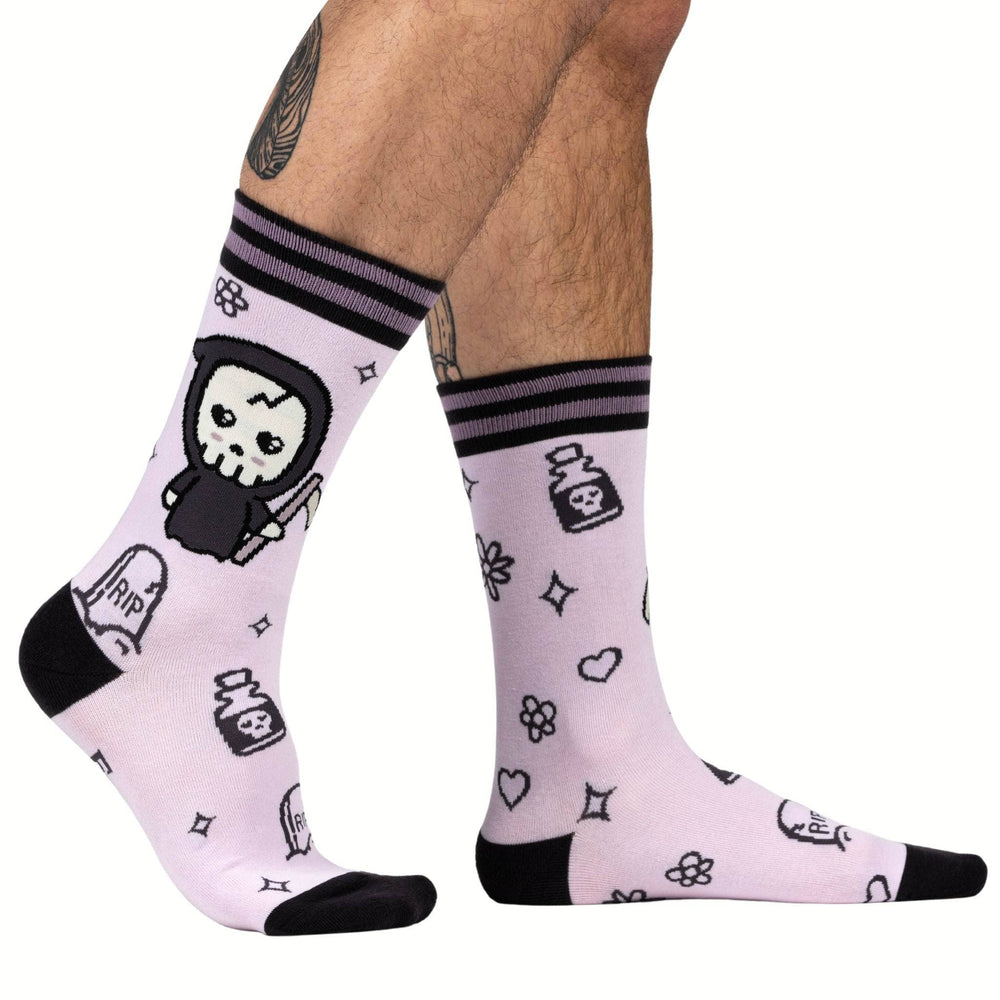 
                      
                        Model wearing a pair of socks depicting a cartoon version of the grim reaper. Pastel pink socks, cute pattern. Black toes, cuff and heel. 
                      
                    