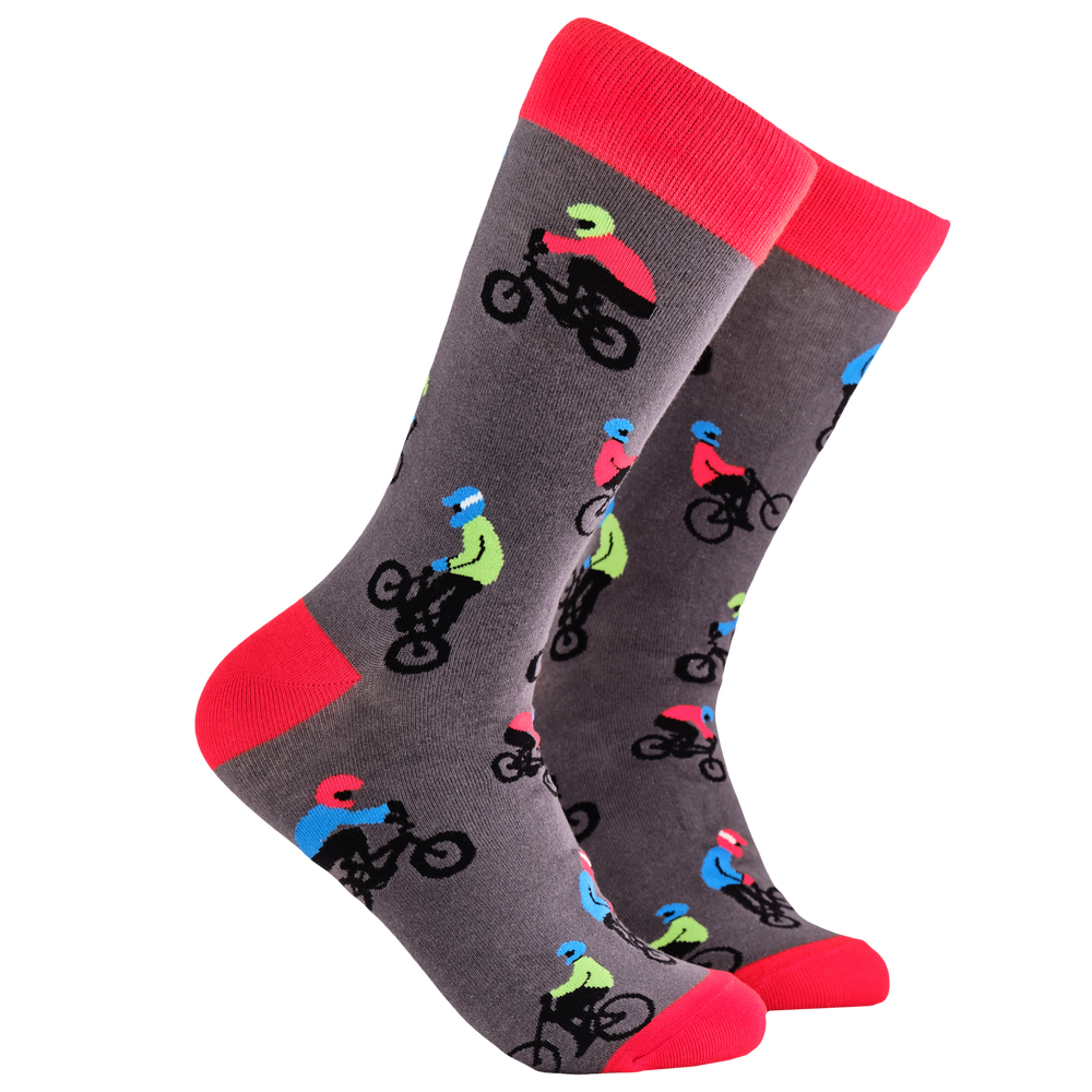 BMX Socks. A pair of socks depicting people riding BMX bikes. Grey legs, red cuff, heel and toe.