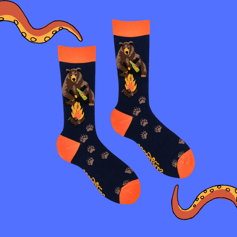 
                      
                        A pair of socks depicting a bear sitting by a campfire. Dark blue legs, orange cuff, heel and toe. 
                      
                    