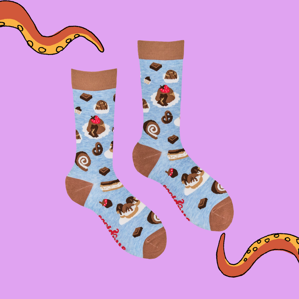 
                      
                        A pair of socks depicting cakes and chocolates. Blue legs, brown heel, toe and cuff. 
                      
                    