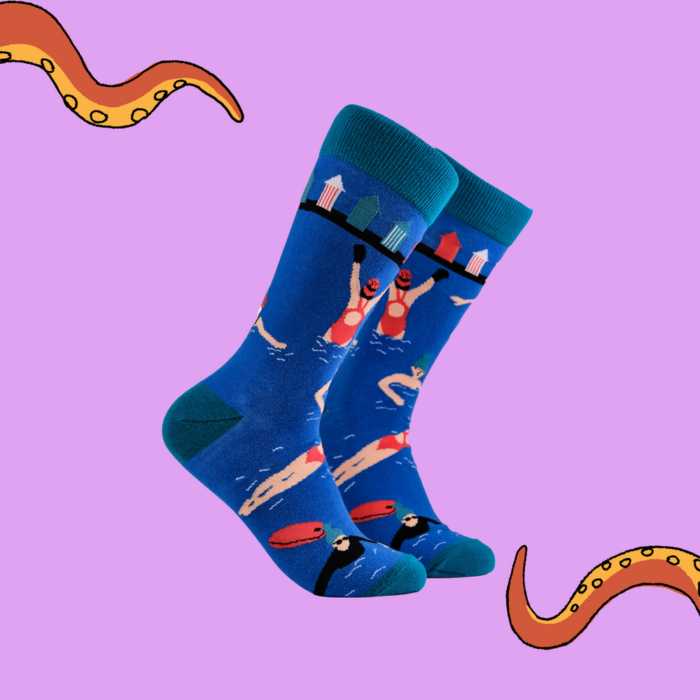 A pair of socks depicting swimmers and beach huts. Blue legs, light blue cuff, heel and toe.