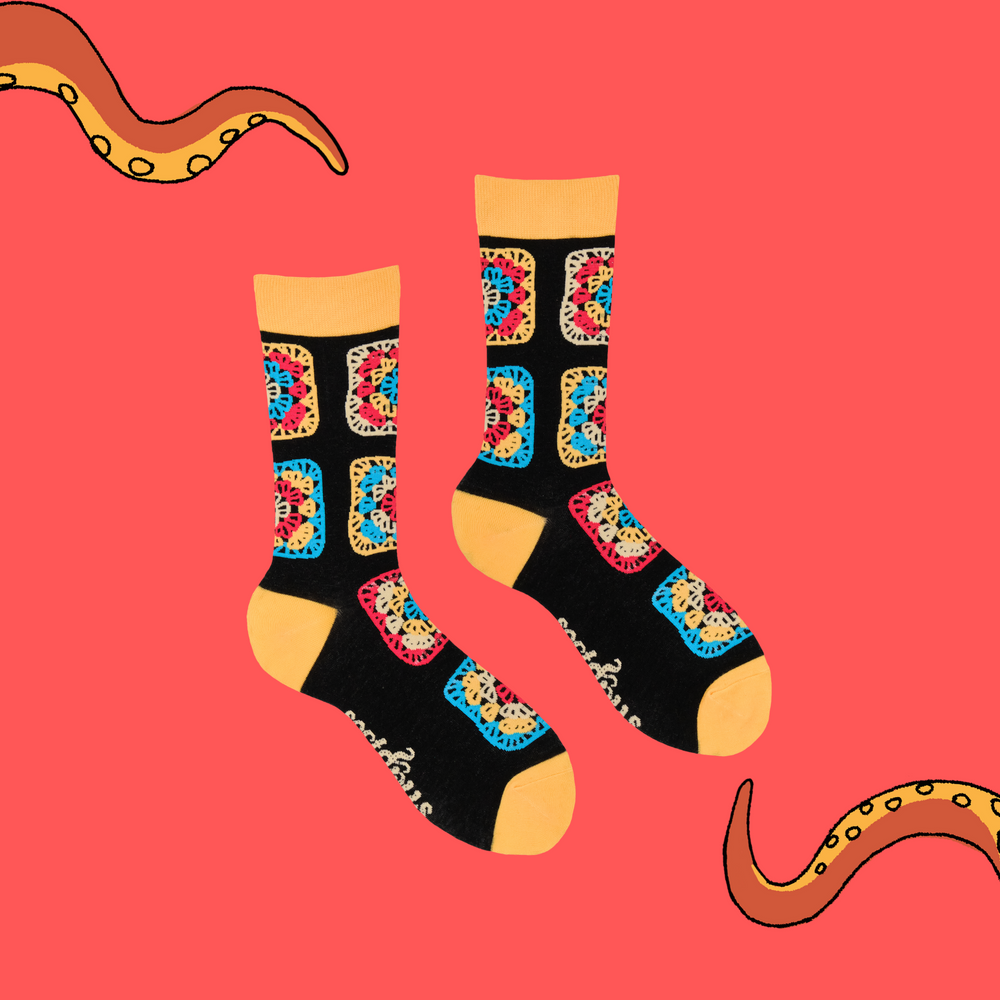 
                      
                        A pair of socks with a multicoloured crochet motif. Black legs, yellow heel, toe and cuff. 
                      
                    