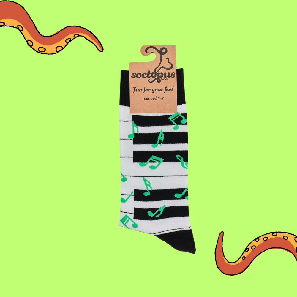 
                  
                    A pair of socks depicting a piano keyboard and green music notes. Black and white piano legs, black cuff, heel and toe. In Soctopus Packaging.
                  
                