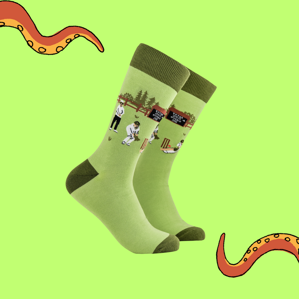 A pair of socks depicting a cricket match. Green legs, dark cuff, heel and toe.