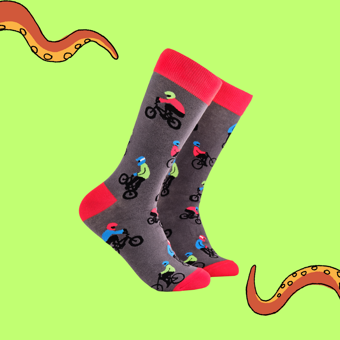 A pair of socks depicting people riding BMX bikes. Grey legs, red cuff, heel and toe.