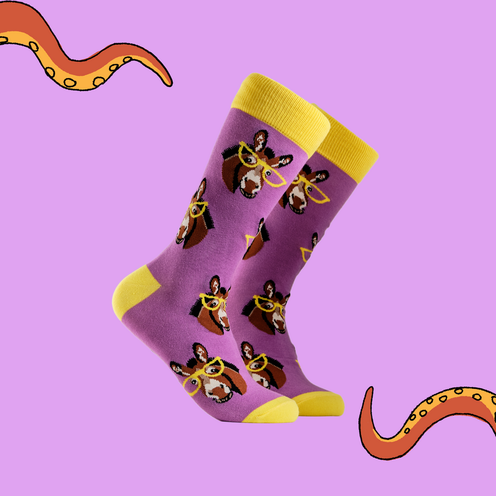 A pair of socks depicting donkeys wearing glasses. Bright pink legs, yellow cuff, heel and toe.