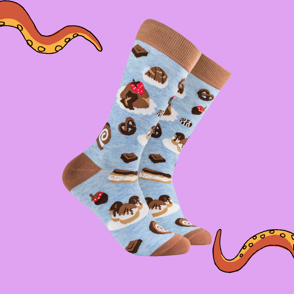 
                      
                        A pair of socks depicting cakes and chocolates. Blue legs, brown heel, toe and cuff. 
                      
                    