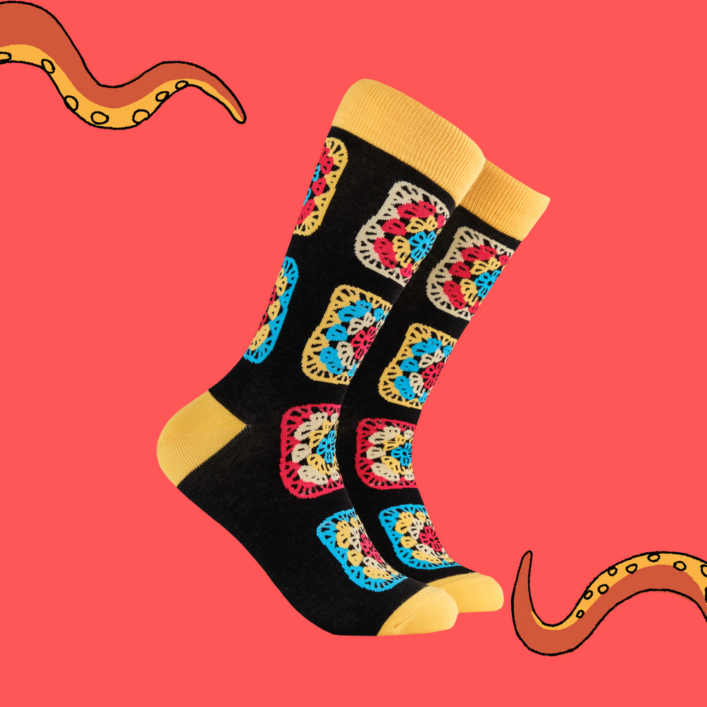 
                      
                        A pair of socks with a multicoloured crochet motif. Black legs, yellow heel, toe and cuff. 
                      
                    