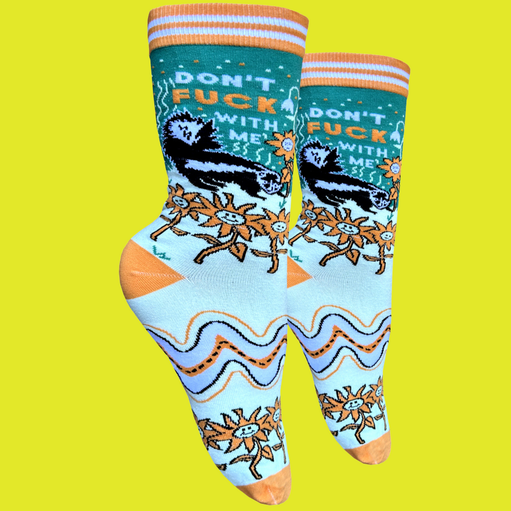 A pair of socks with a bold sweary slogan and trippy pattern of flowers and a skunk. Orange toes, heel and cuff.