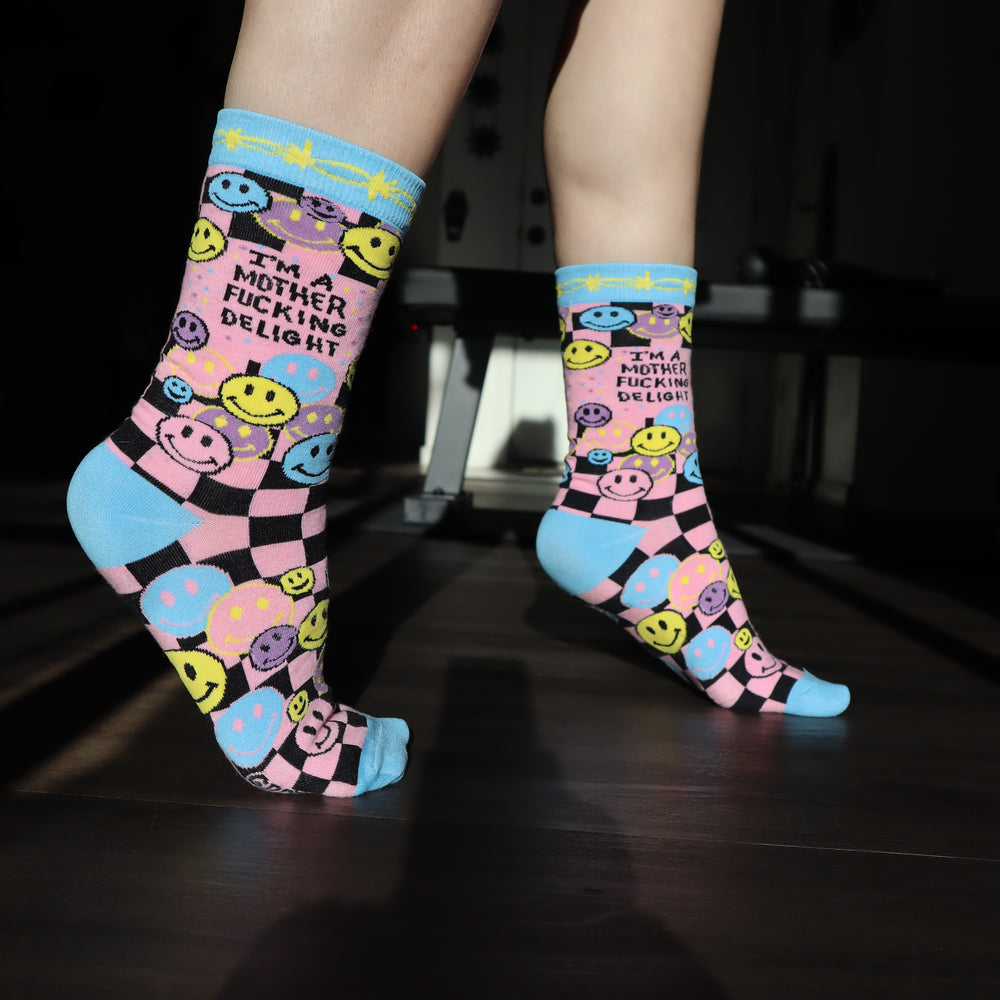 
                  
                    Model wearing a pair of socks with a bright pink and blue smiley face pattern and a bold sweary slogan. Blue toes, heel and cuff.
                  
                