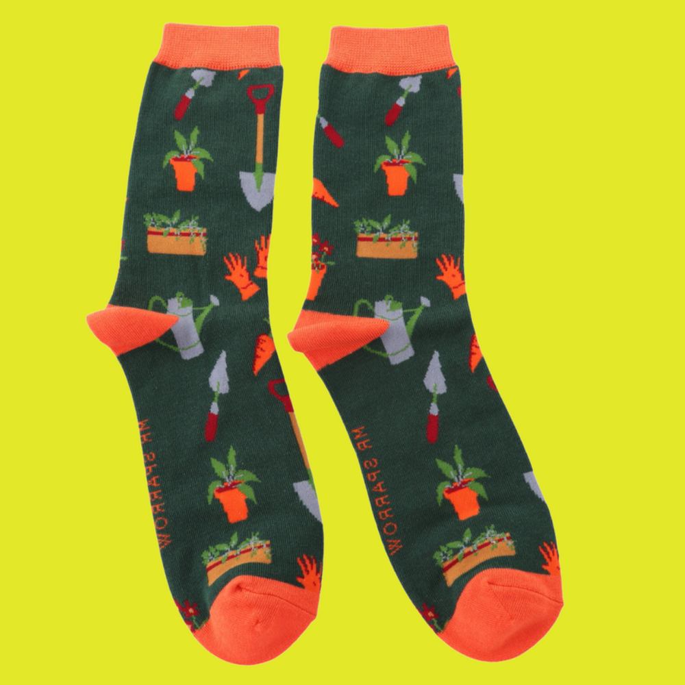 
                      
                        A pair of socks featuring gardeners tools, dark green legs, orange heel, toe and cuff. 
                      
                    