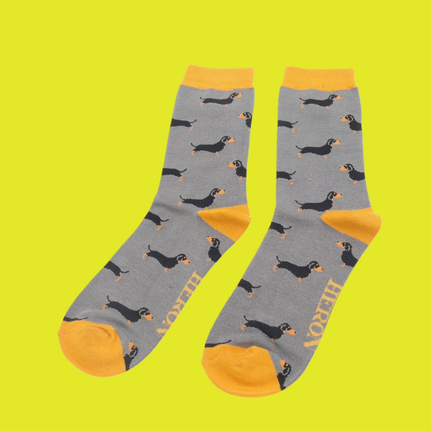 
                  
                    A pair of socks featuring a sausage dog pattern. Grey legs, yellow cuffs, heel and toe.
                  
                