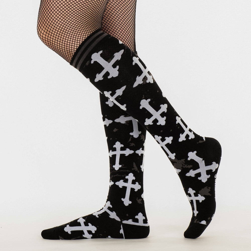 
                      
                        A model wearing a pair of knee high socks with a gothic cross pattern. Black and white. 
                      
                    