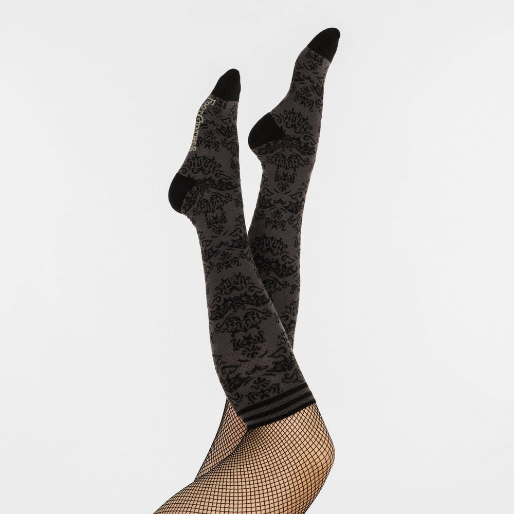 
                      
                        A model wearing a pair of knee high socks with a bat and damask pattern. Grey legs, black, heel, toe and cuff. 
                      
                    