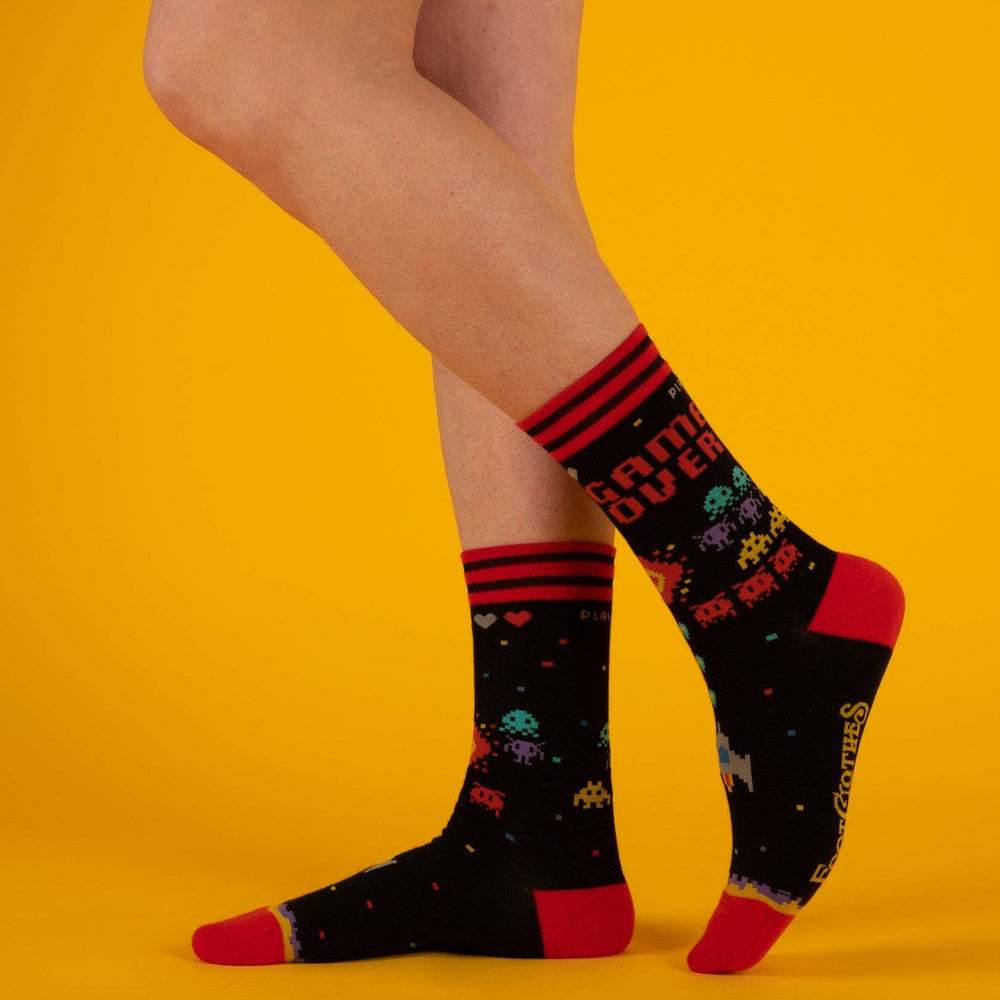 
                      
                        A model wearing a pair of socks featuring space invaders and game over. Black legs, red heel, toe and cuff. 
                      
                    