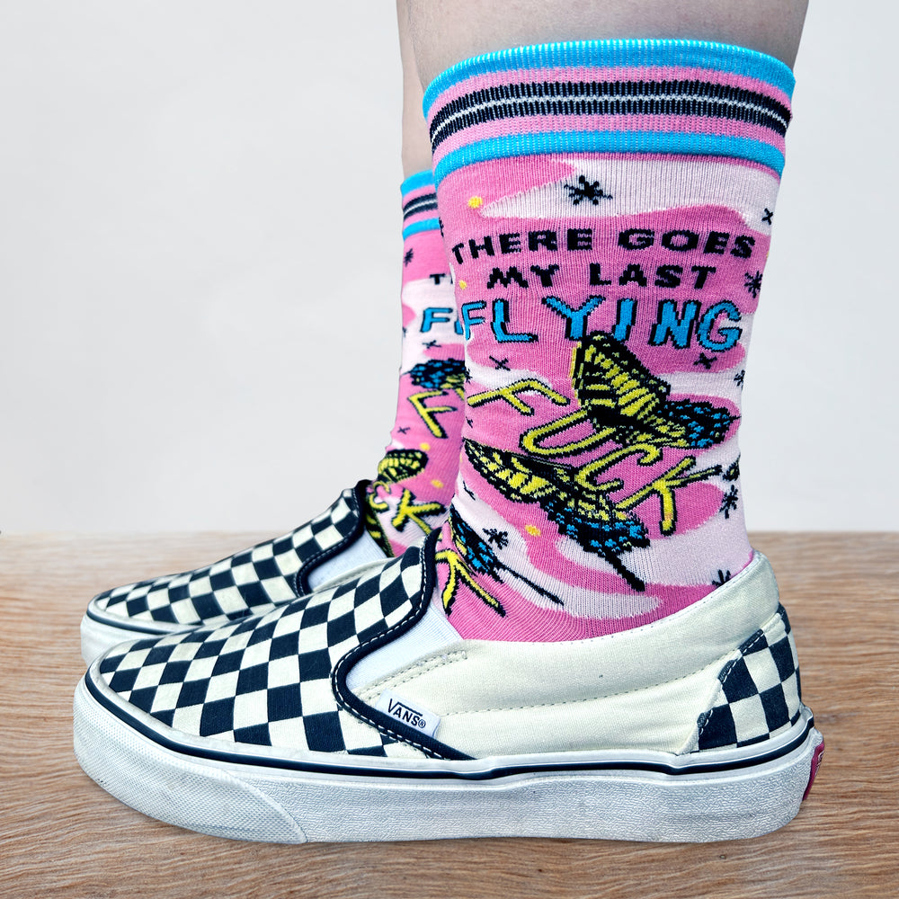 
                      
                        Last Flying F**k Socks - Small. Model wearing a pair of socks with a bold slogan and a pink and yellow butterfly motif. Bright blue heel, toe and cuff.
                      
                    